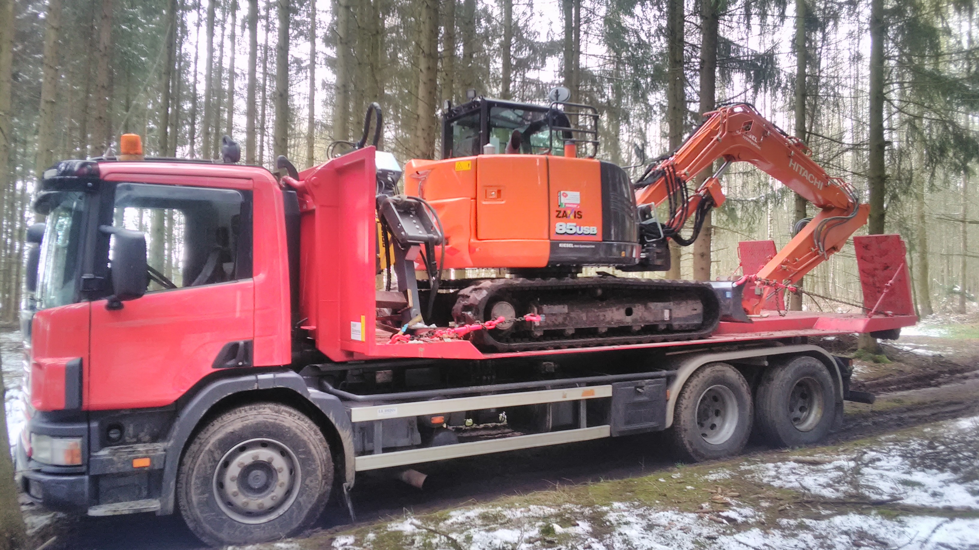 Zu sehen ist unser LKW Abrollkipper mit Transportplattform auf dem unserer Bagger Hitachi ZX 85 steht